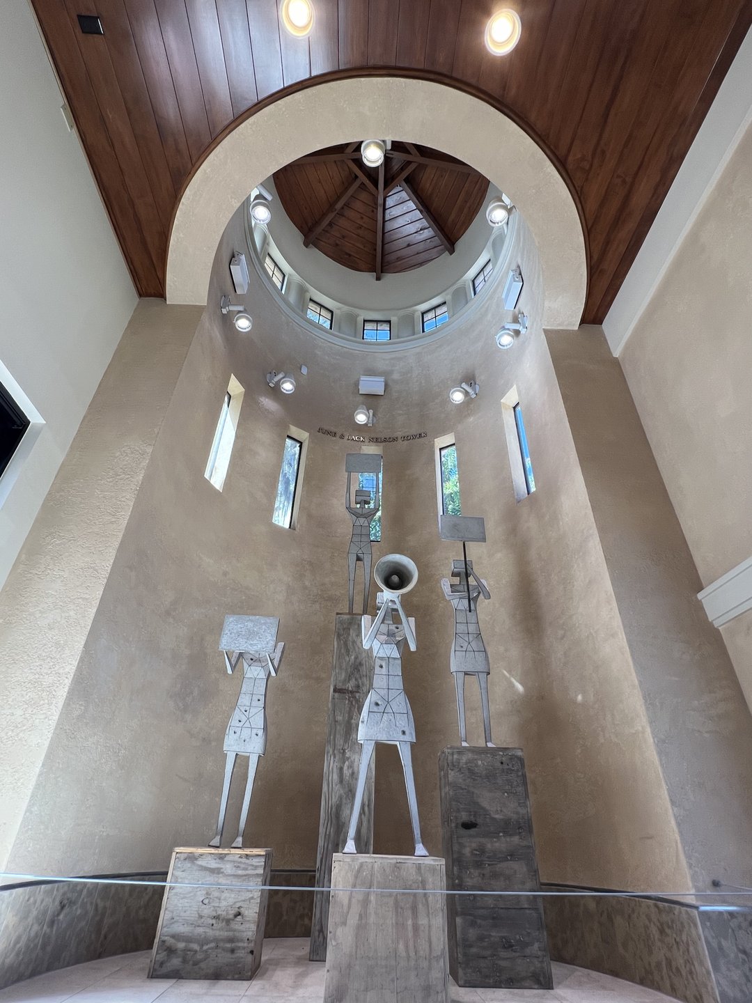 Three abstract metal sculptures stand on stone pedestals in a circular atrium with a high wooden ceiling and natural light streaming in.