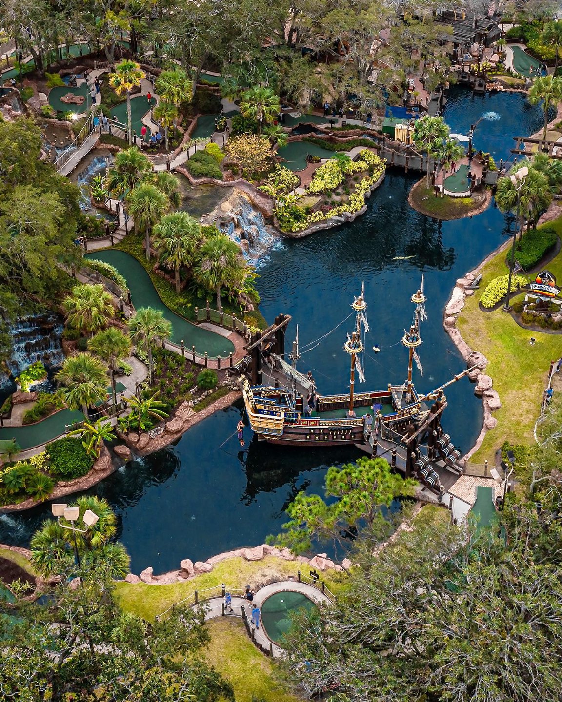 Aerial view of a lush, tropical landscape featuring a winding waterway, a pirate ship, and vibrant greenery, inviting exploration and adventure.