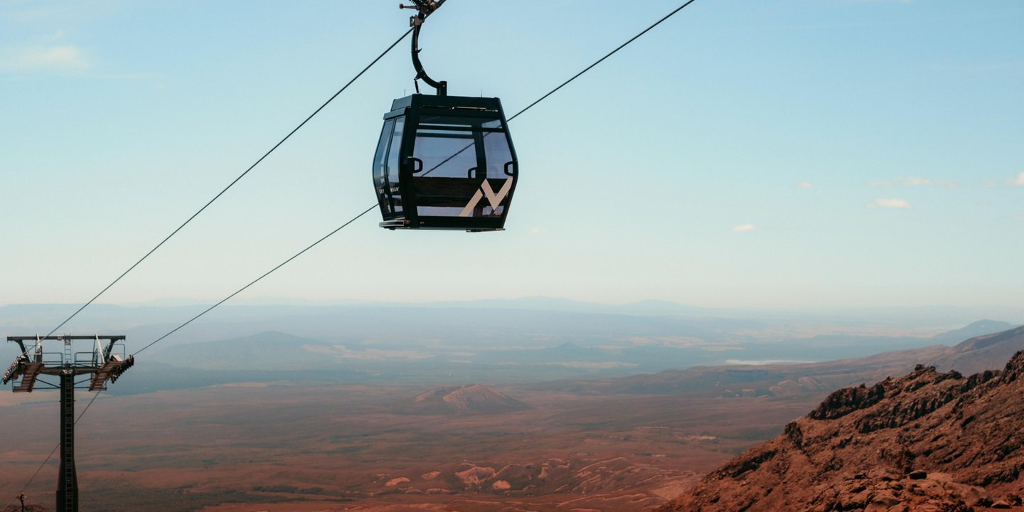A cable car glides above a vast, arid landscape with distant mountains under a clear blue sky, offering scenic views.
