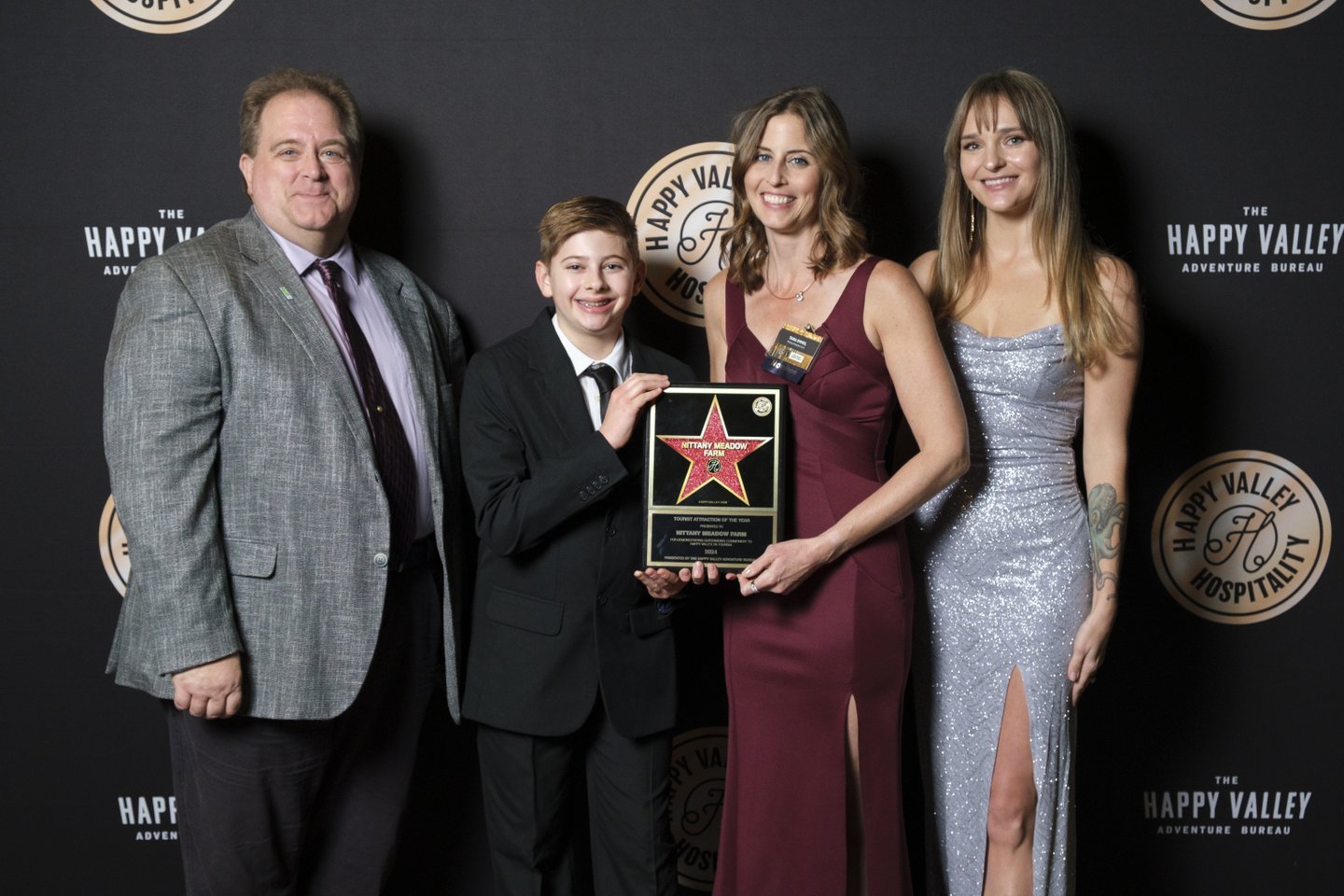 A group of four people stands together, holding an award plaque against a dark backdrop featuring a logo for Happy Valley Hospitality.