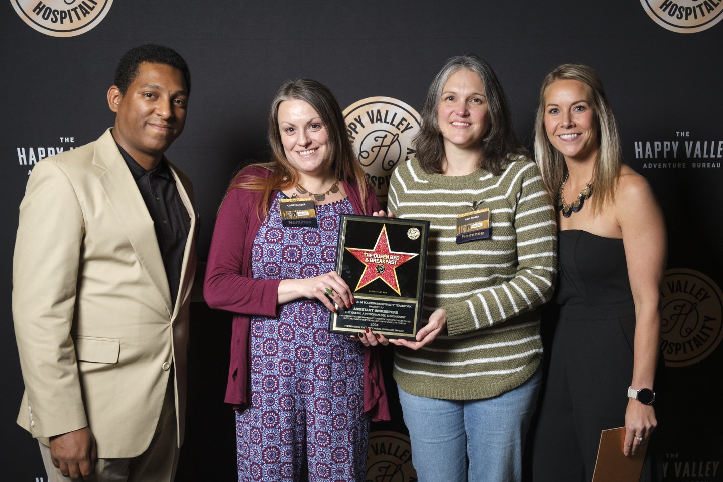 Four individuals stand together, holding an award plaque against a dark backdrop with logos. They are dressed in formal attire, smiling.