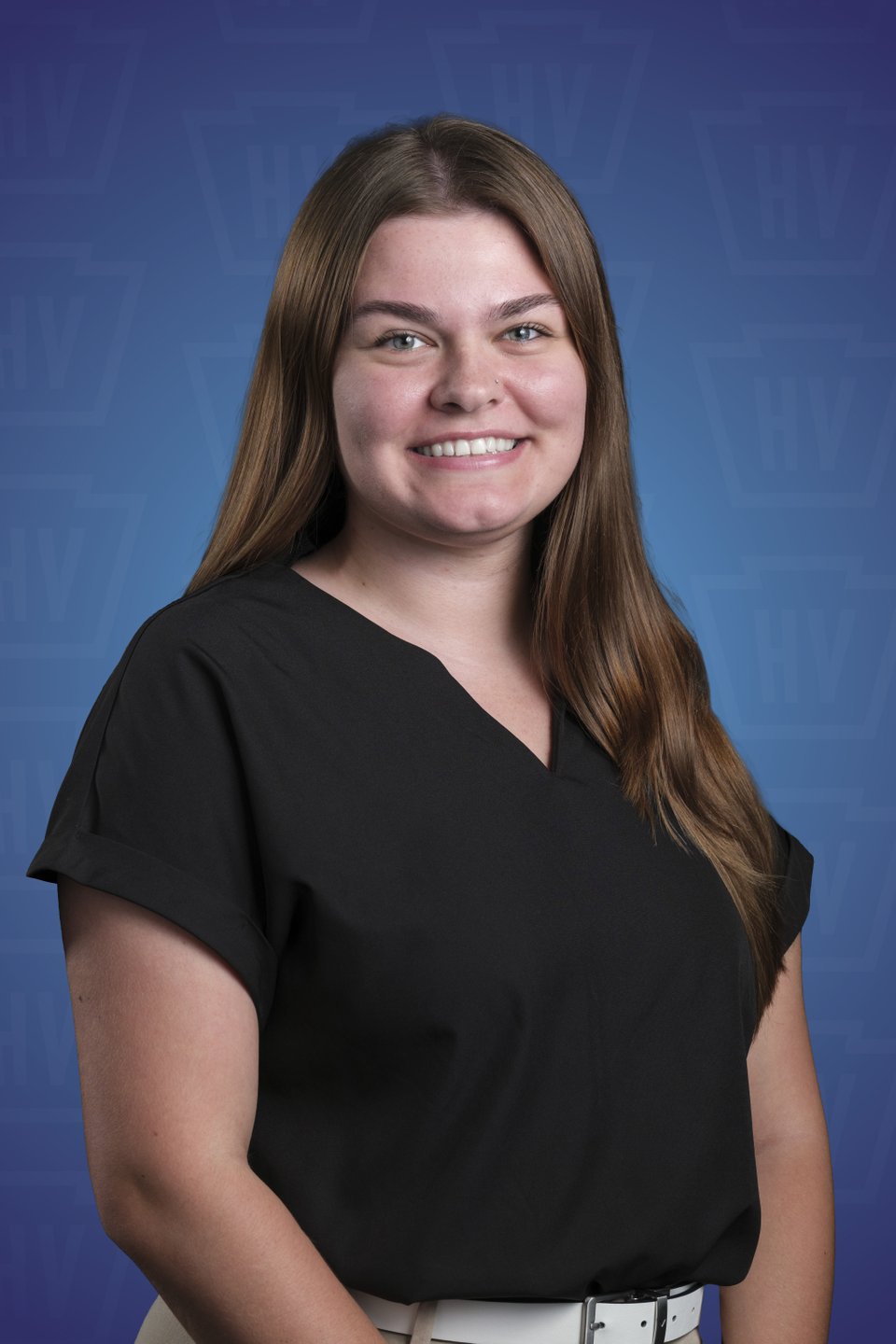 A smiling young woman with long brown hair, wearing a black top, poses against a blue background with a subtle pattern.