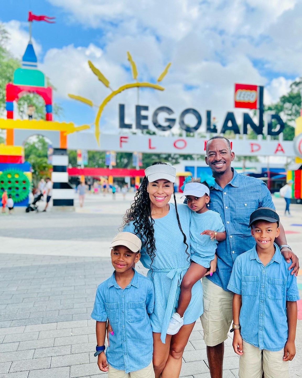 A family of four stands in front of the colorful LEGOLAND Florida entrance, featuring vibrant structures and a sunny sky.