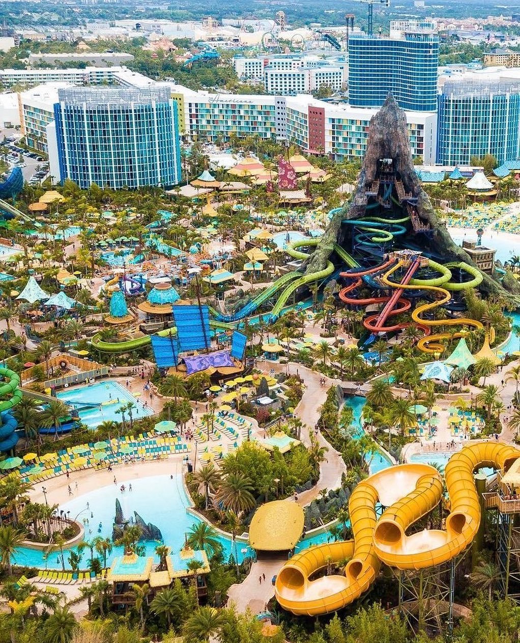Aerial view of a vibrant water park featuring colorful slides, pools, and lush landscaping, surrounded by hotels and attractions.