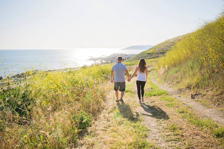 Couple walking hand in hand away from the camera on a sunny coastal path