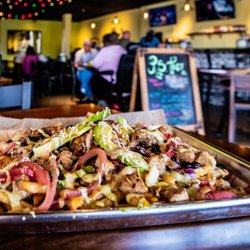 A vibrant platter of loaded nachos topped with chicken, vegetables, and cheese, set in a lively restaurant with patrons in the background.
