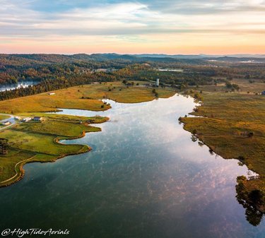 Aerial view of a serene landscape featuring a winding river reflecting the sky, surrounded by lush greenery and distant hills.
