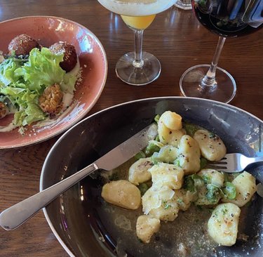 A plate of gnocchi with herbs and sauce, accompanied by a salad and two cocktails. A glass of red wine is also visible.