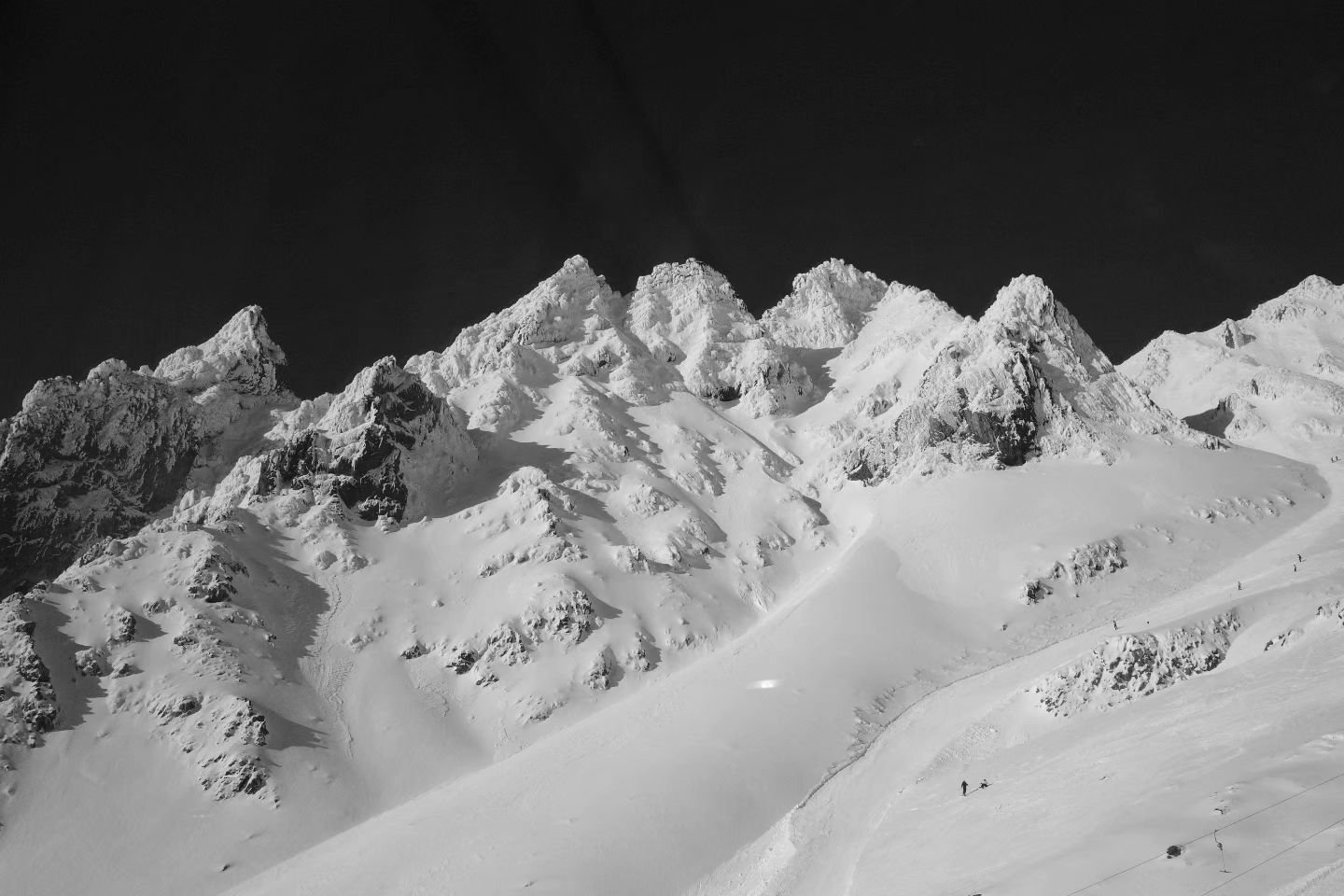 Snow-covered mountain peaks rise sharply against a dark sky, with a winding path visible below. Two small figures traverse the snowy landscape.