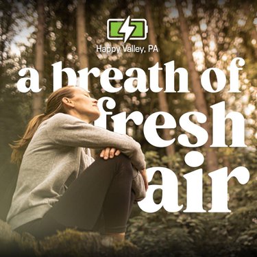 A woman sits peacefully in a forest, surrounded by trees, enjoying the tranquility. Text overlay reads, "a breath of fresh air."