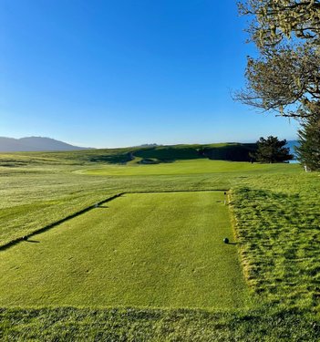A scenic golf course tee box with lush green grass, rolling hills, and a clear blue sky in the background, inviting outdoor recreation.