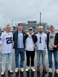 Five friends stand together in a parking lot, wearing sports jerseys, with a large stadium in the background under a cloudy sky.
