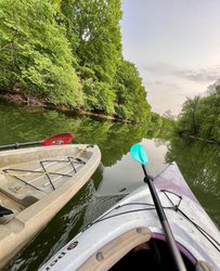 Two kayaks float on a calm, green river surrounded by lush trees. The scene captures a serene outdoor experience, ideal for exploration.