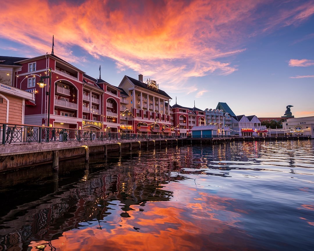 Colorful sunset over a waterfront with charming buildings reflecting in the water. A serene atmosphere invites exploration and relaxation.