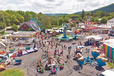 A vibrant outdoor fairground filled with colorful rides and attractions. Crowds enjoy various activities under a bright sky, surrounded by green hills.