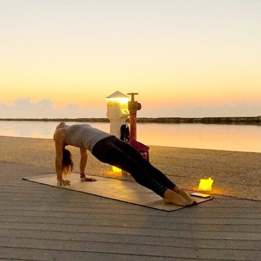 A person practicing yoga on a mat by a calm waterfront at sunset, with soft lighting and a serene atmosphere enhancing relaxation.