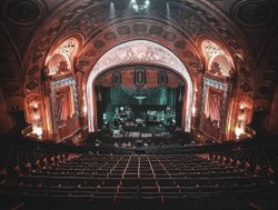 Ornate theater interior with a grand stage, intricate ceiling details, and empty seating. Soft lighting highlights the elegant decor.