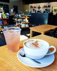 A cozy café scene featuring a frothy cappuccino and a refreshing iced drink on a wooden table, with a vibrant shop backdrop.