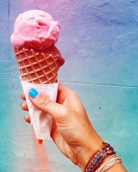 A hand holds a waffle cone with two scoops of pink ice cream against a colorful, gradient background. The scene evokes a refreshing treat.