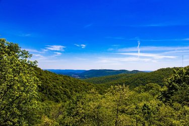 Lush green hills stretch under a bright blue sky, with distant mountains visible on the horizon, creating a serene natural landscape.