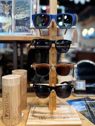 Display of sunglasses on a wooden stand, featuring four styles: blue, black, brown, and tortoiseshell. Bamboo containers are nearby.