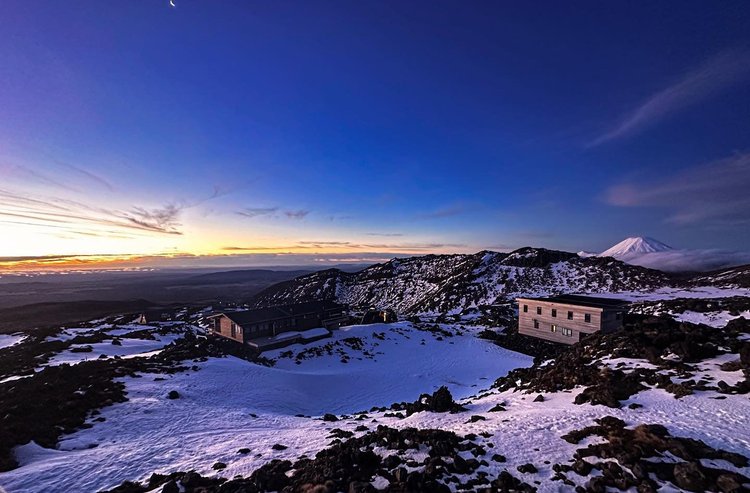 Snow-covered landscape at sunset, featuring rustic lodges against a backdrop of mountains. A serene, expansive view invites exploration.