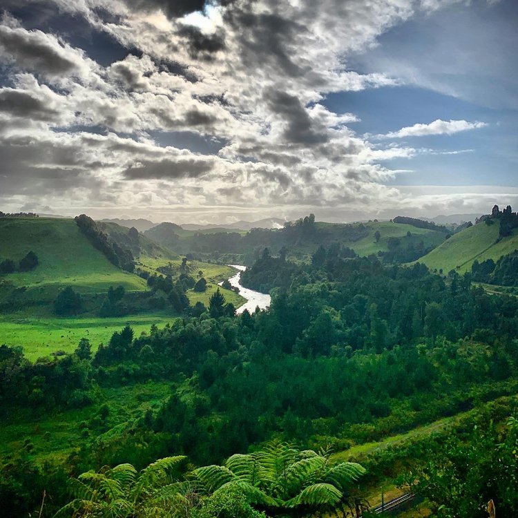 Lush green hills and a winding river under a partly cloudy sky create a serene landscape. Ideal for outdoor exploration and relaxation.