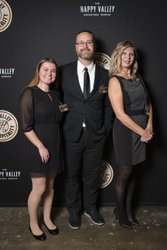 Three individuals stand together in formal attire against a dark backdrop featuring "The Happy Valley Adventure Resort" logo.