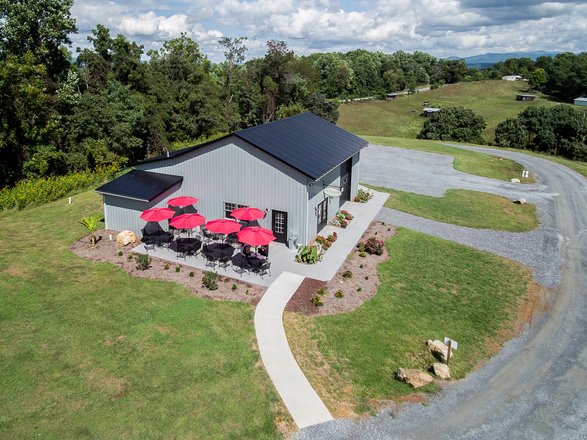 A modern building with a black roof and red umbrellas on a patio, surrounded by green grass and trees under a partly cloudy sky.
