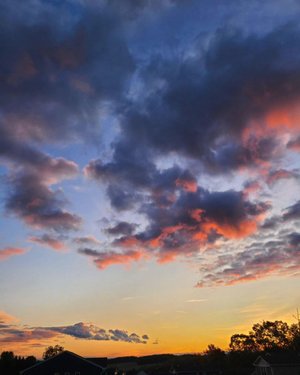 Vibrant sunset sky with clouds in shades of orange, pink, and purple, casting a serene atmosphere over a tranquil landscape.
