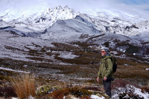 A hiker stands in a snowy landscape, with majestic mountains in the background. The scene captures the rugged beauty of nature.