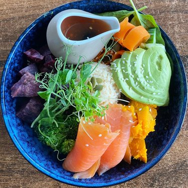 A vibrant bowl of fresh sushi ingredients, featuring salmon, avocado, and colorful vegetables, served with a small sauce container.
