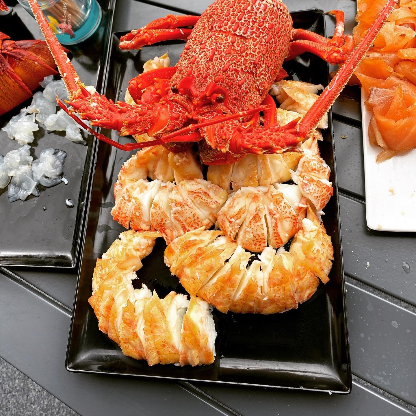 A vibrant platter featuring a whole cooked lobster atop succulent lobster tails, surrounded by fresh seafood delicacies on a sleek black tray.