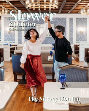 A couple dances joyfully in a stylish dining area with elegant decor and blue glassware, promoting a relaxed atmosphere at The Nittany Lion Inn.
