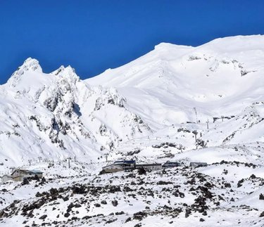 Snow-covered mountains rise against a clear blue sky, with ski lifts and lodges nestled in the valley below, inviting winter activities.