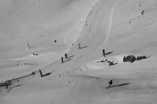 Skiers navigate a snowy slope under a clear sky, with ski lifts in the background and rocky outcrops scattered across the landscape.