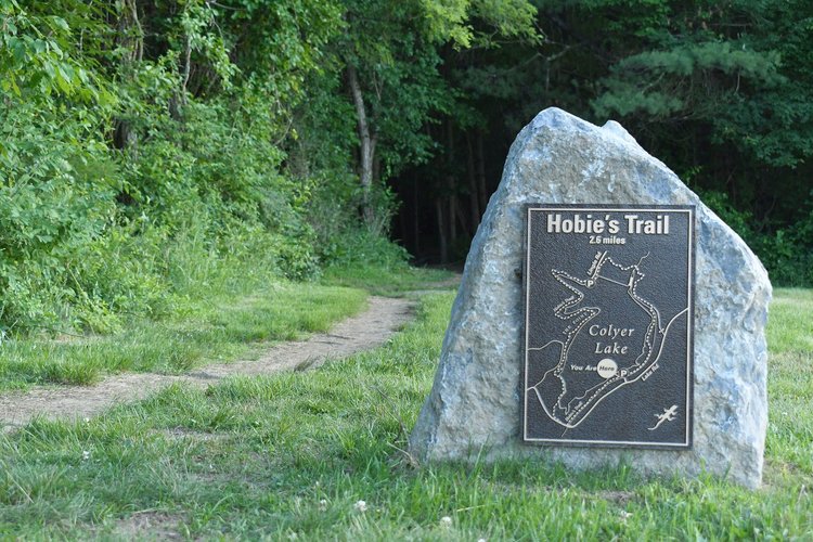 Sign marking Hobie's Trail, 2.6 miles to Colyer Lake, with a gravel path leading into a lush green forest. Ideal for outdoor exploration.